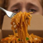 A close-up of a fork twirling clumped Pad Thai noodles