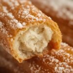 A close-up of a golden-brown churro dusted with cinnamon sugar,