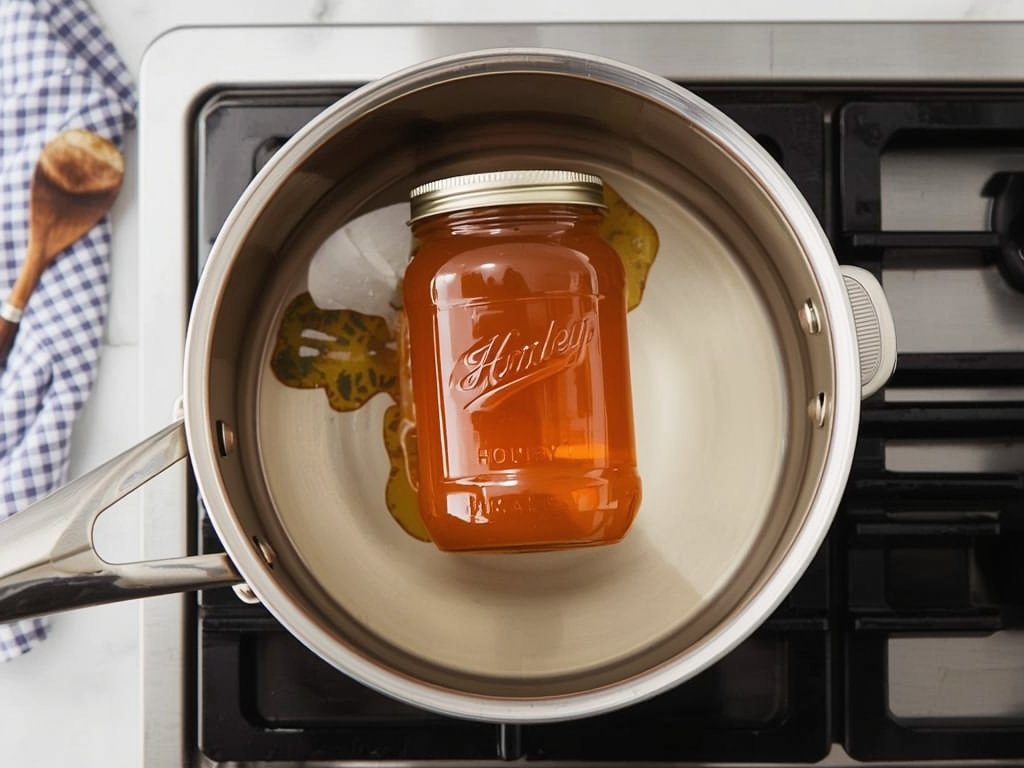 A glass jar of honey being gently warmed in a