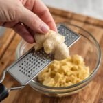 A hand holding a frozen ginger root over a microplane